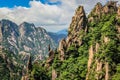 Sharp rocks with bright green trees leading from top right to bottom left with distant rocky mountain peaks on the left